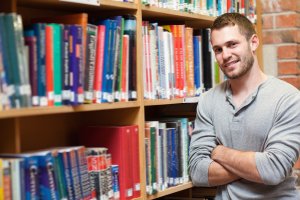 Smiling male student leaning on a shelf in a library