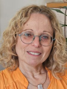 תמונה של ד"ר לילך בן משה געש, קרימינולוגית קלינית, מטפלת, מדריכה ומרצה בתכנית תואר שני לטיפול באמצעות אמנויות - טיפול בפסיכודרמה. לבושה בחולצה כתומה